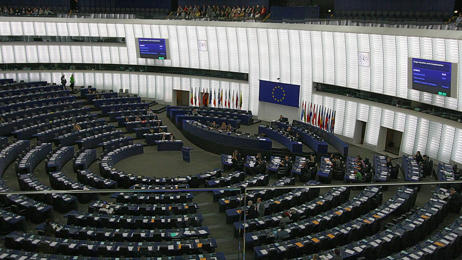 The plenary chamber of the European Parliament in Strasbourg, with rows of blue seats, the EU flag and the flags of member states